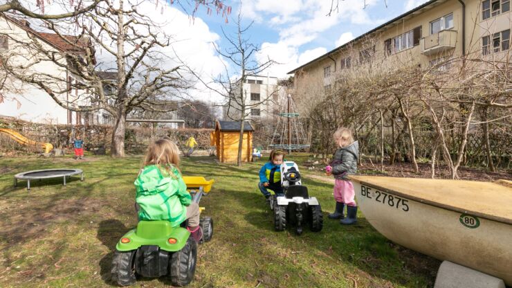 Spielende Kinder im Garten der Kita Soleil mit Trampolin, Rutschbahn, Schaukel, Kletterturm und Spielzeugtraktore.