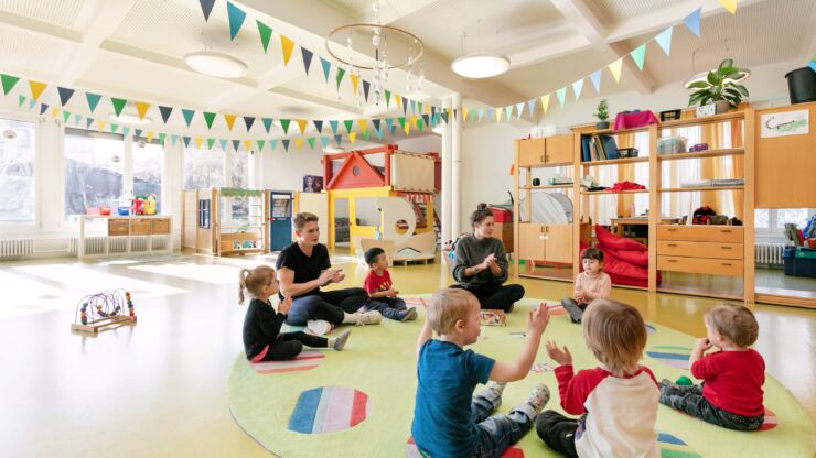 Kinder und Betreuungspersonal sitzen in einem Kreis und singen.