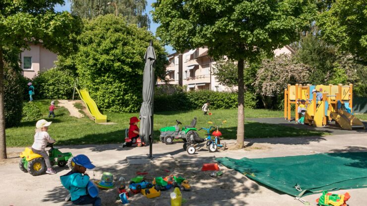 Spielende Kinder mit Traktor und sonstigen Spielsachen im Garten der Kita Mett