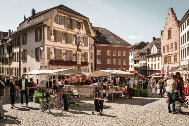 Viele Leute flanieren auf dem Burgplatz in der Bieler Altstadt zwischen den Marktst&auml;nden. Man sieht den Gerechtigkeitsbrunnen und mehrere Fr&uuml;chte- und Gem&uuml;sest&auml;nde.