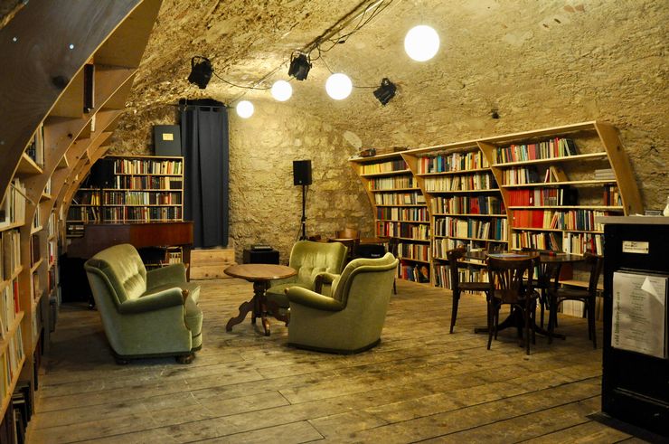 Dans une pièce avec un plancher de bois et des murs de pierre, il y a beaucoup de livres sur les étagères et divers styles de sièges, ainsi qu'un système de musique.