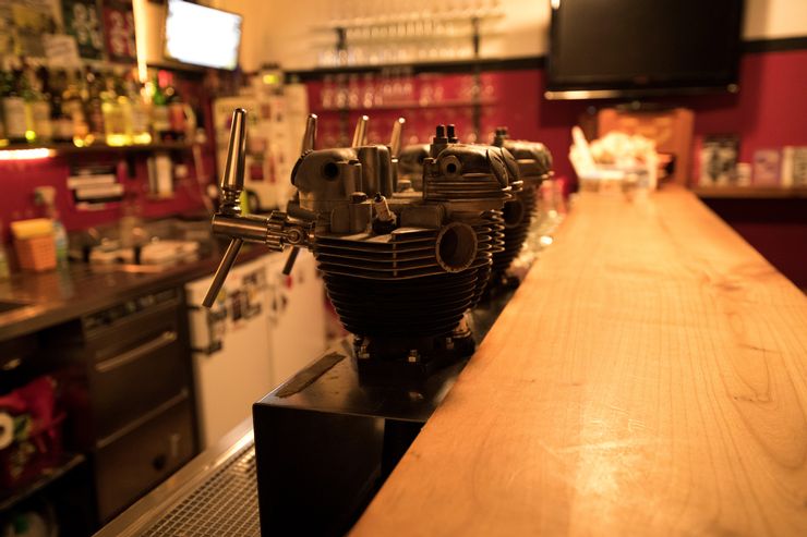 Dans un bar à la thèse, on voit au premier plan différents robinets de bière et derrière eux des bouteilles, des verres et différents placards. 