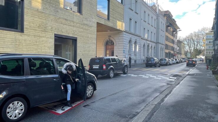 Eine Frau steigt aus einem Auto. Mehrere parkierte Autos stehen entlang der Strasse.