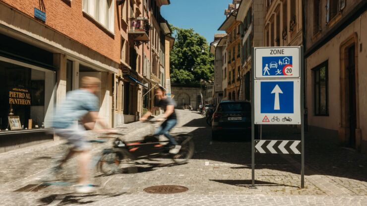 Deux cyclistes se croisent au panneau indiquant la zone de rencontre de la Vieille Ville. 