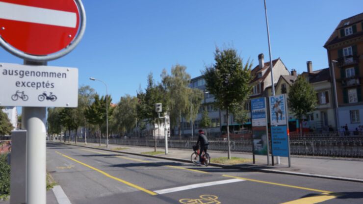 Ein Velofahrer fährt auf dem Velostreifen, links ist eine Verkehrstafel, die den Gegenverkehr für Zweiräder erlaubt.