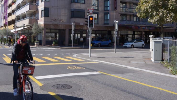 Des marquages jaunes sur la rue pour les cyclistes devant un feu rouge, à gauche un cycliste longe la rue.
