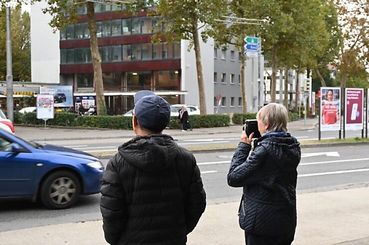 Deux personnes sont debout à côté de la rue; une femme regarde par un appareil photo. 