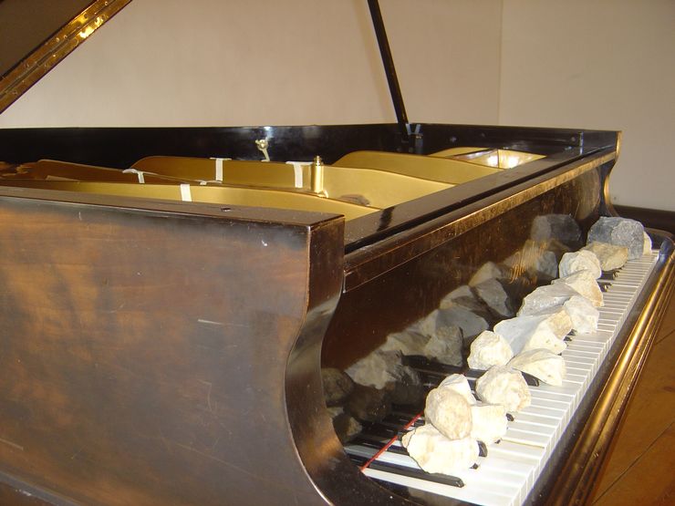 Auf einem braun-goldenen Klavier liegen Steine auf der Klaviatur. 