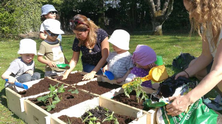 Kinder bepflanzen zusammen mit Betreuerinnen ein Hochbeet mit Gemüse.