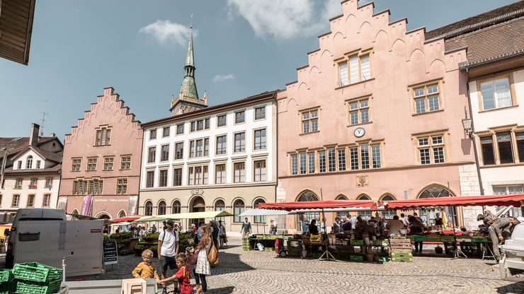 Das Bild zeigt einige Stände des Gemüsemarktes auf dem Burgplatz in der Altstadt, umringt von historischen Altstadthäusern.