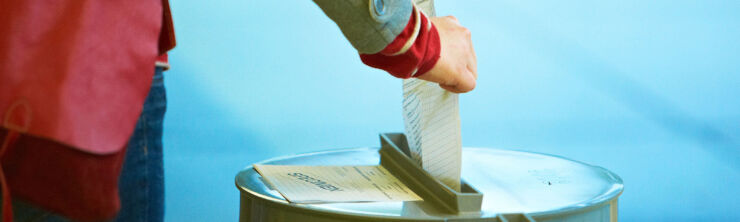 Une personne, dont on ne voit que la main, glisse un bulletin de vote dans une urne