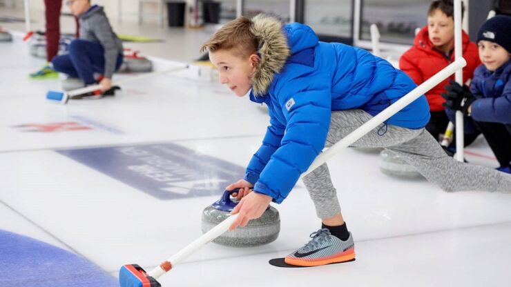 Ein Knabe übt sich auf dem Eisfeld im Curlingsport